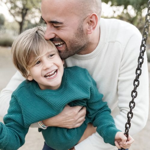 Happy dad and son having fun in city park swinging on swing - Main focus on father eye