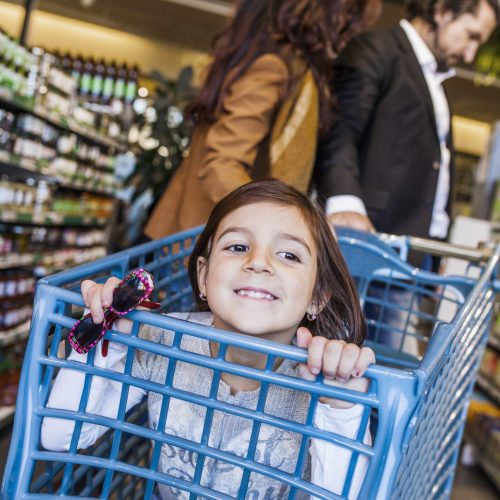 Happy girl sitting in cart with parents at supermarket