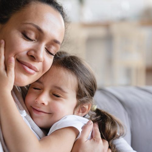 Young caucasian mother and little daughter hugging embracing with eyes closed, expressing love and care. Family moments together, parenthood and motherhood concept. Happy Mother`s day!